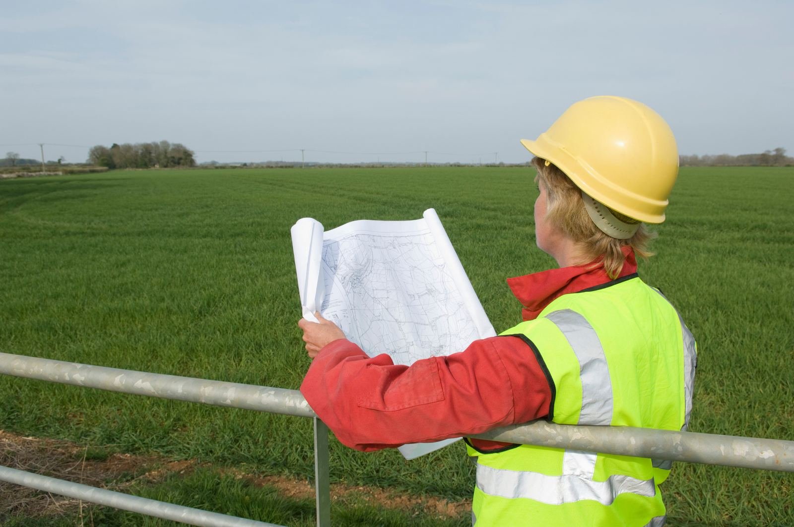 Surveyor reviewing design plans over an open field site