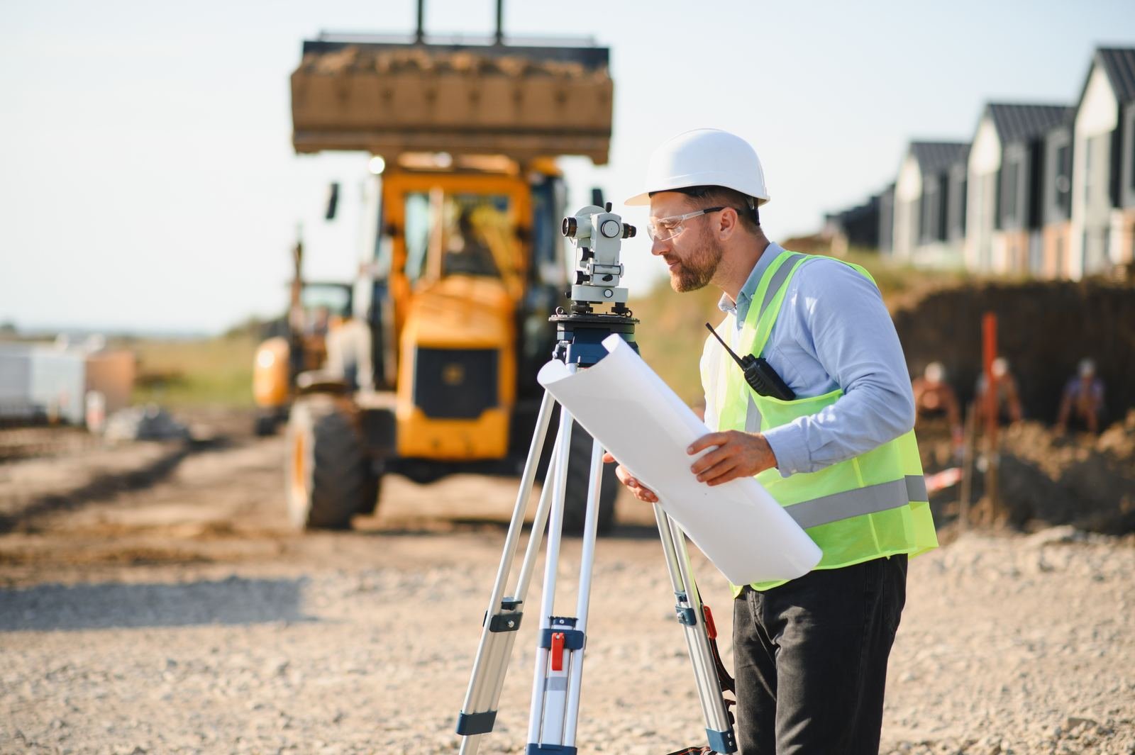 Surveyor with rolled site plans next to a theodolite and an excavator